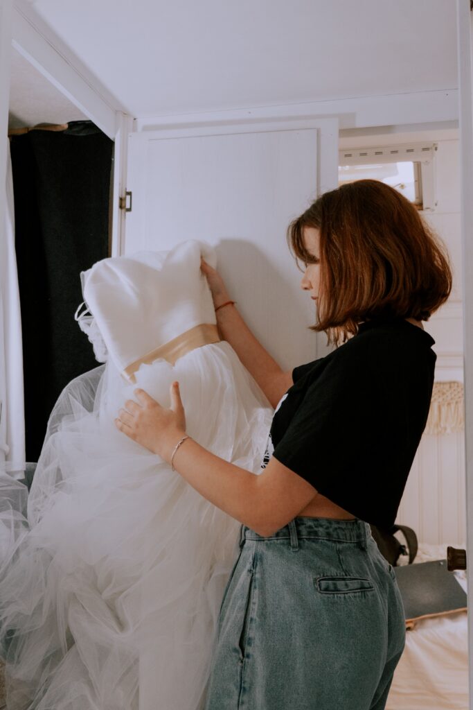 A young woman closely examines a beautiful wedding dress inside a room.